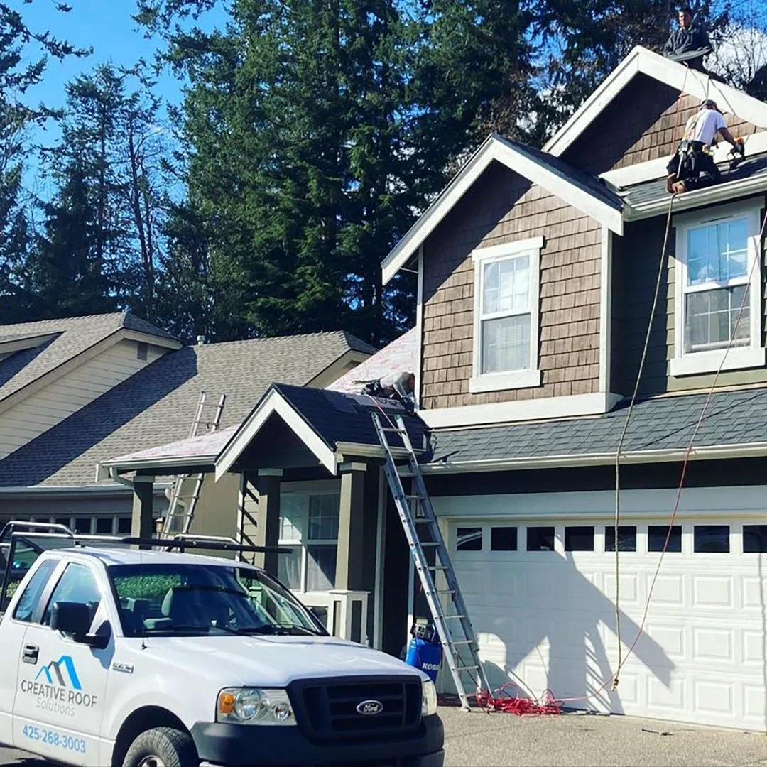 Roofing crew replacing a home's roof with ladders and a Creative Roof Solutions truck outside.