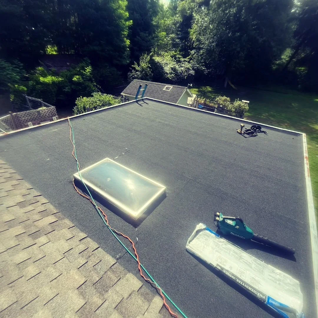 Flat roof with skylight, roofing materials, and tools during installation.