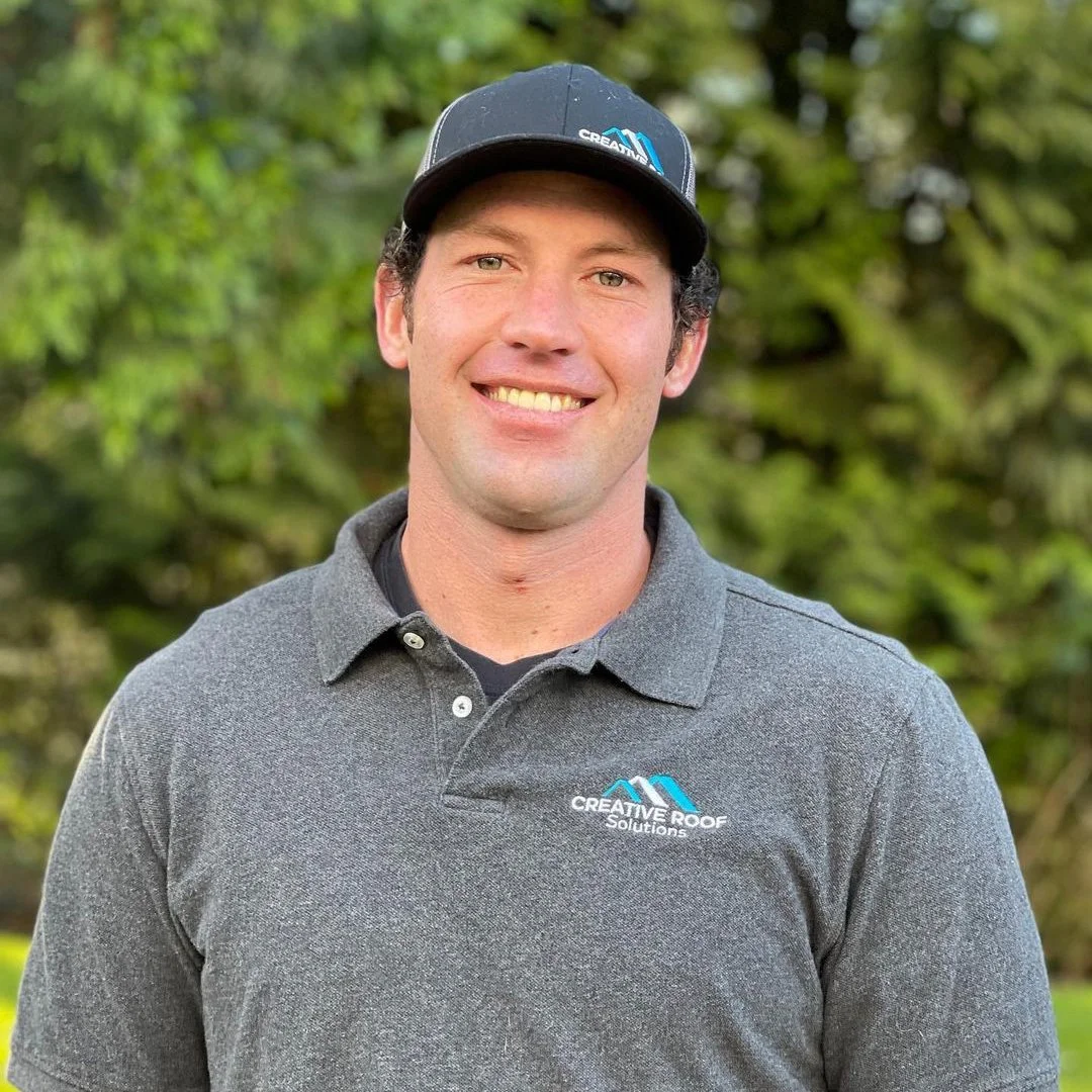 Creative Roof Solutions team member wearing a branded gray polo and black company cap outdoors.