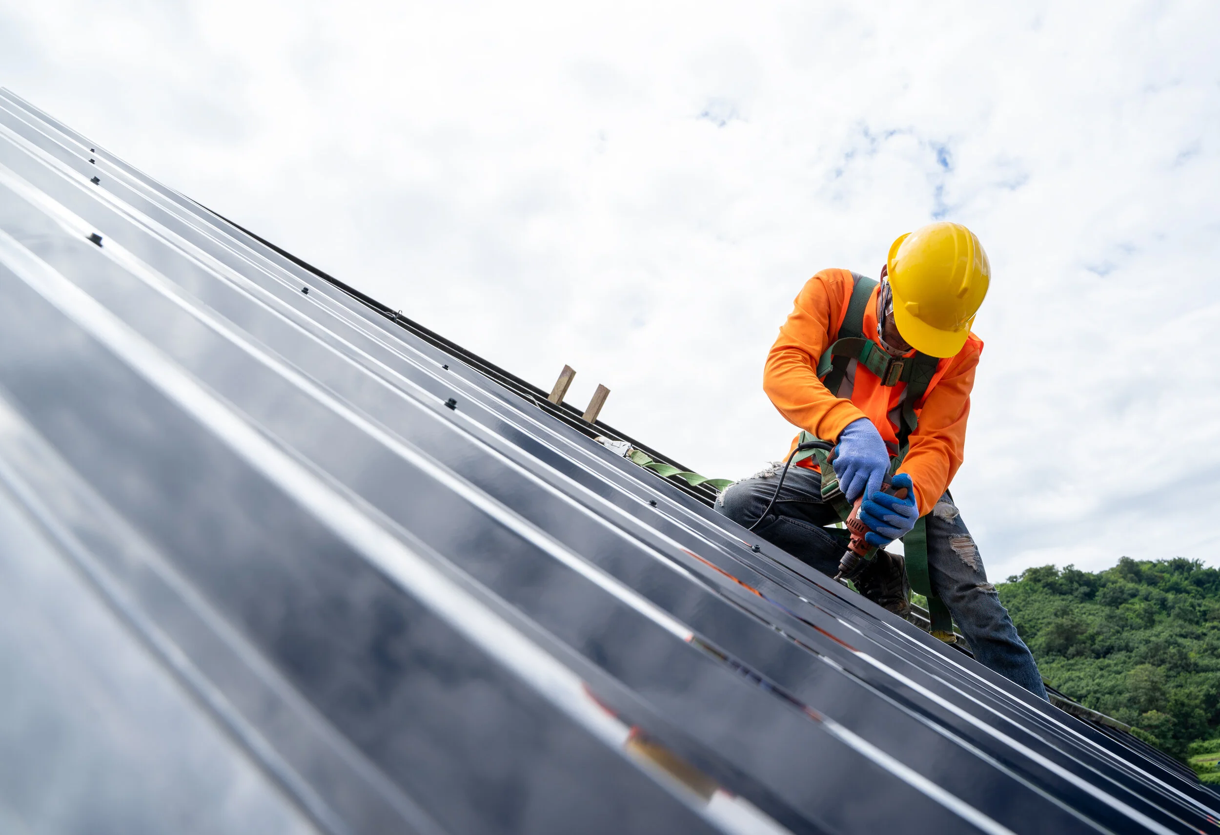 Worker installing a standing seam metal roof while wearing a safety harness and hard hat.