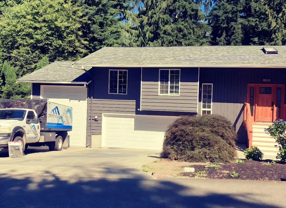 Gray two-story home with a new roof and a Creative Roof Solutions truck in the driveway.