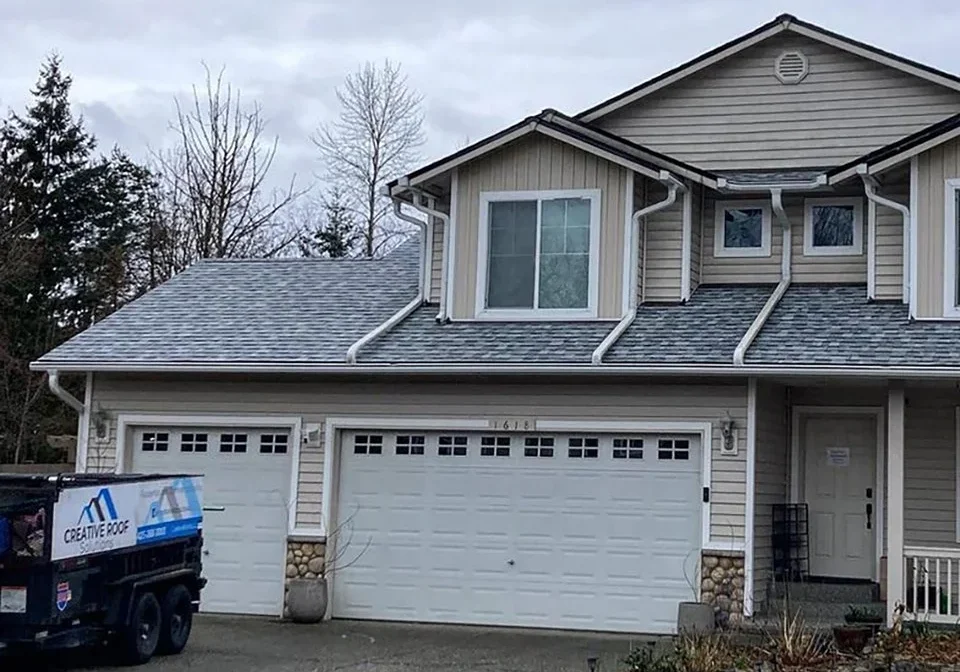 Two-story home with a newly installed gray shingle roof and Creative Roof Solutions trailer.