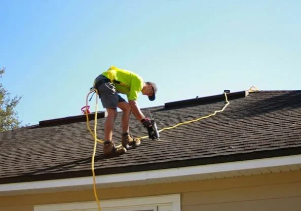 Roofer using a nail gun to install asphalt shingles on a residential roof