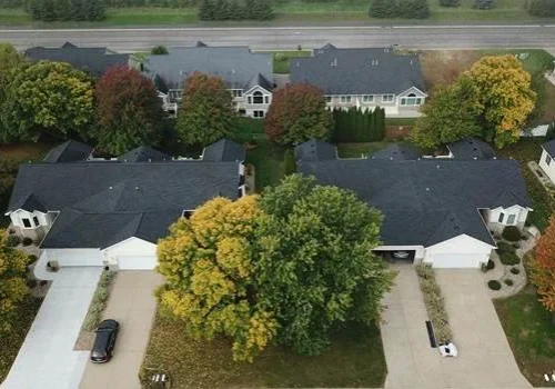 Aerial view of neighboring homes with newly installed dark gray roofs and autumn trees