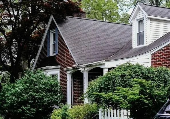 Traditional brick home with a gray shingle roof, front porch, and mature landscaping
