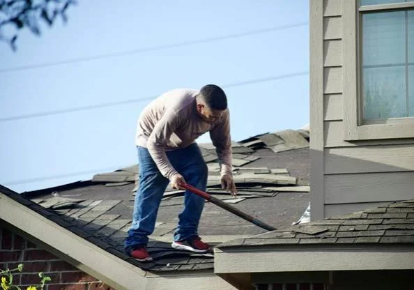 Contractor removing worn asphalt shingles from a residential roof during replacement