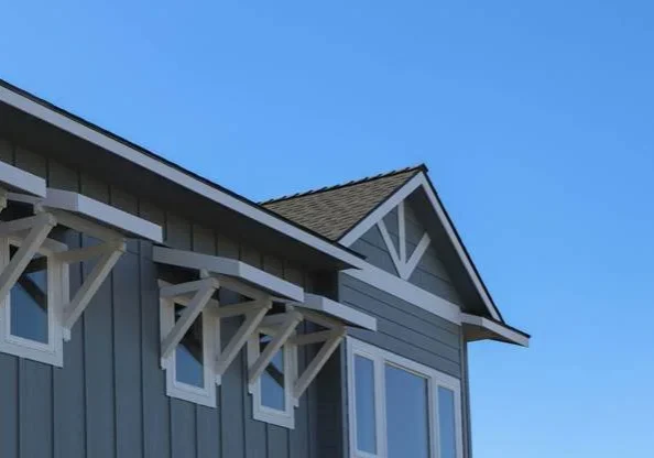 Gray home with a dark asphalt shingle roof and decorative gable under a clear blue sky