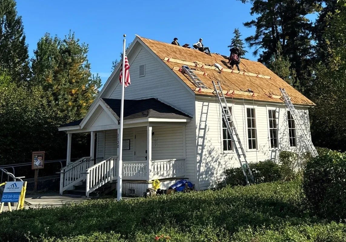 Roofing crew replacing the roof on a white historic building with ladders and safety equipment.