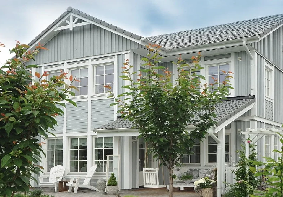 Two-story home with a gray tile roof, white trim, and rain gutters surrounded by landscaping