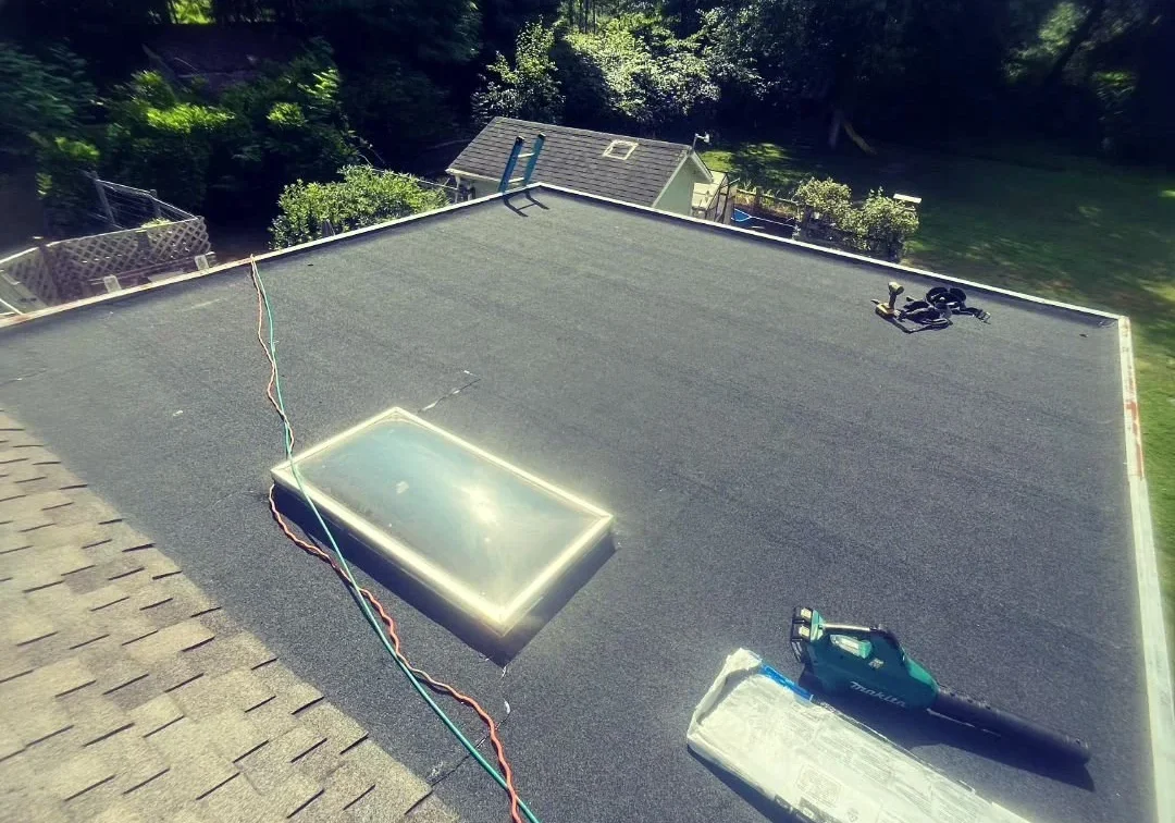 Flat roof with skylight, roofing materials, and tools during installation.