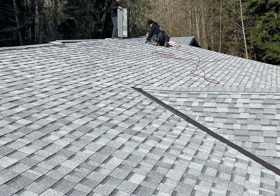 Roofers installing gray architectural shingles on a residential roof.